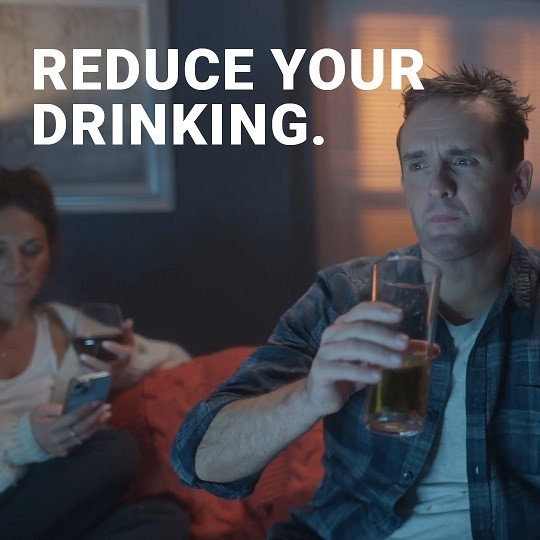 Man drinking beer at home. Text says reduce your drinking