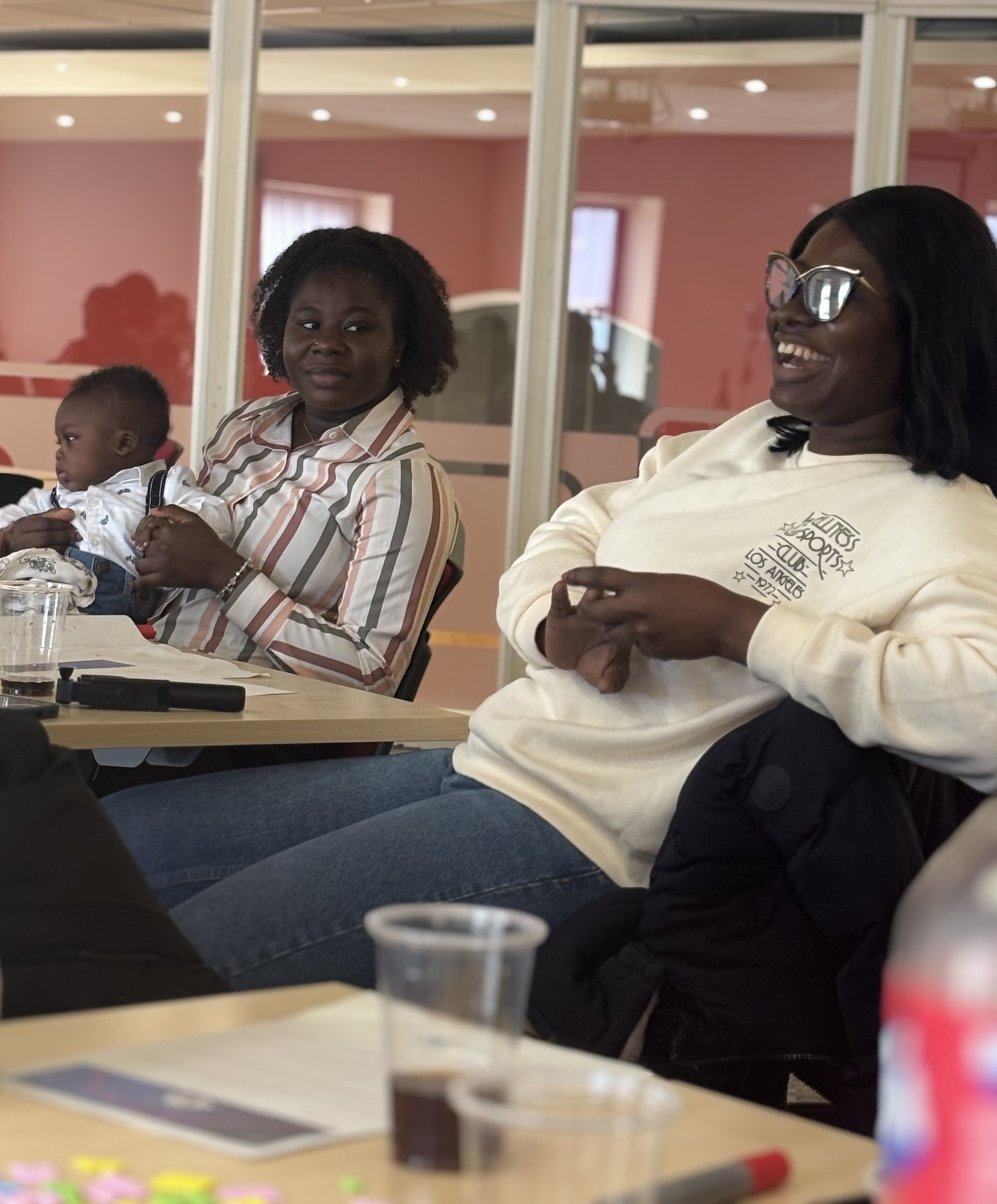 Two women smiling sat at a conference on chairs