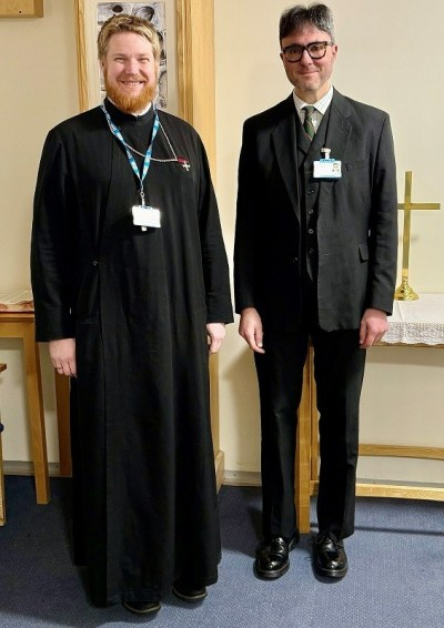 Two men in black smiling in chapel