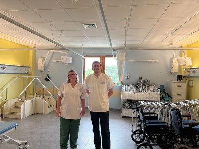 A man and a woman in whiter scrubs smiling in a ward area
