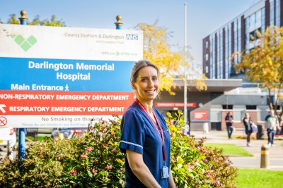 Nurse in uniform smiling outside hospital sign