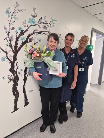Woman holding flowers with two midwives smiling on a ward