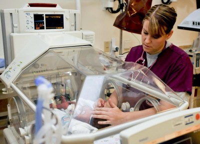 Baby in incubator with nurse in scrubs next to it