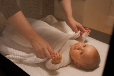 Baby in travel cot being tucked in by dad with blanket