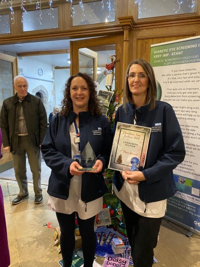 Two women in blue fleeces holding an award and a certificate smiling