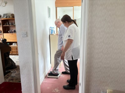 Man on scales in bedroom supported my physiotherpist in white