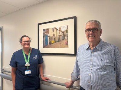 Man and woman smiling on ward next to a framed photo