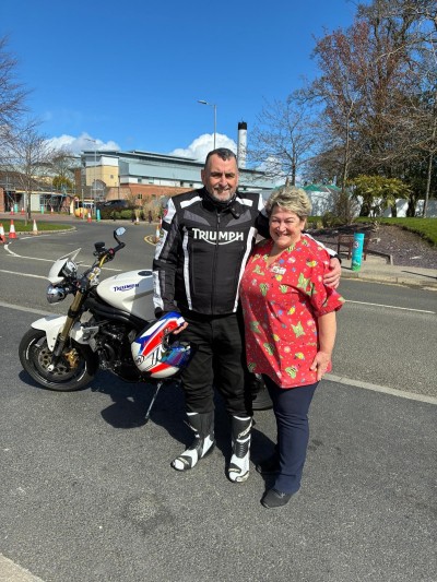 Man in leathers standing by a bike woman in scrubs smiling