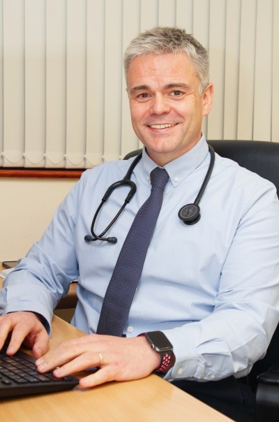 Man in shirt with stethescope round neck sat at a desk